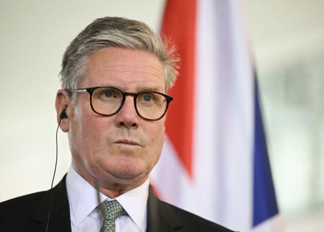 Sir Keir Starmer with an ear piece in his right ear standing in front of a Union flag