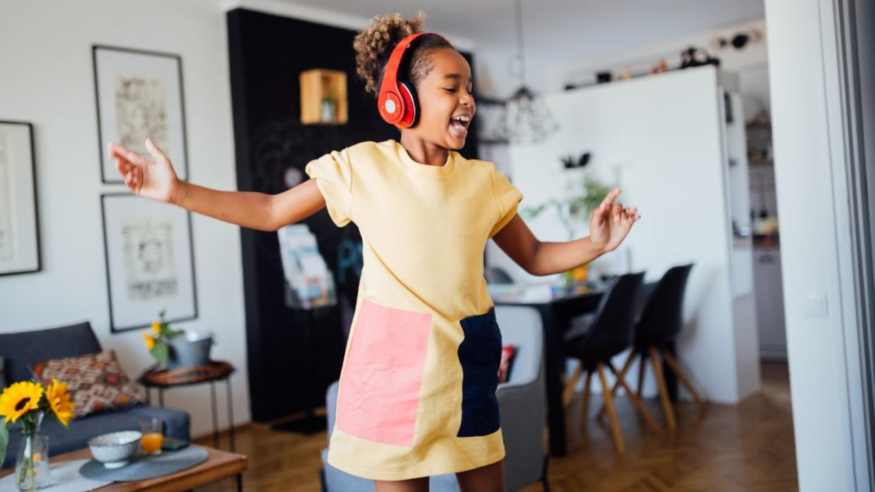 young happy african american girl dancing at home in her living room, wearing headphones, listening to music, having fun and learning the moves