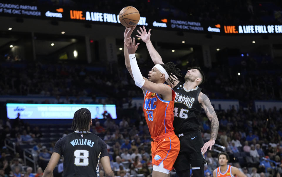 Oklahoma City Thunder forward Ousmane Dieng (13), shoots between Memphis Grizzlies forward Ziaire Williams (8) and guard John Konchar (46) in the first halfof an NBA basketball game Sunday, April 9, 2023, in Oklahoma City. (AP Photo/Sue Ogrocki)