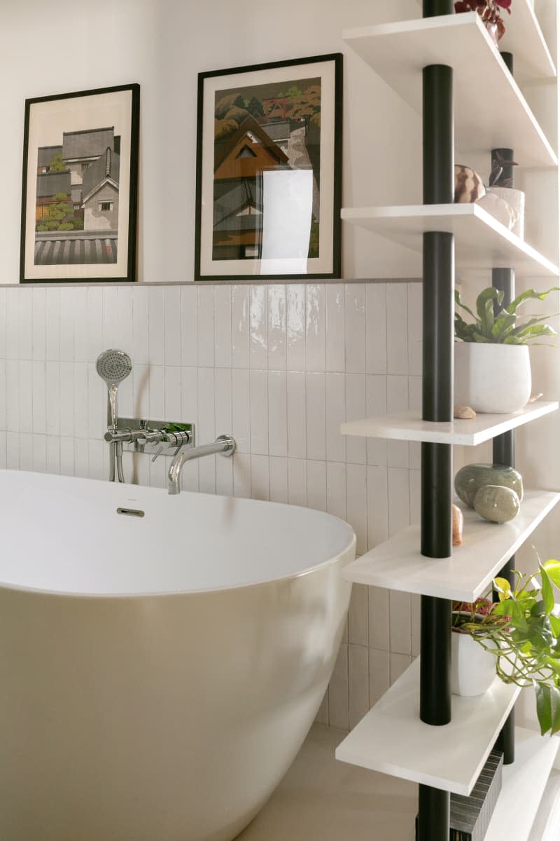 Modern soaking tub, modern floating shelves with plants on display, subway tile up half wall