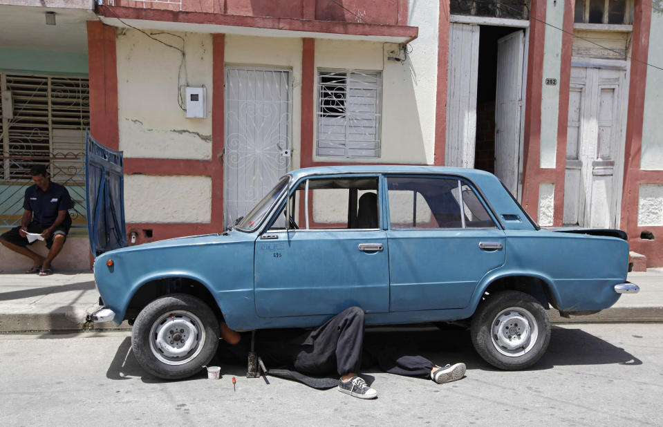 In this photo taken Monday April 23, 2012, a man climbs under the engine of his Russian-made car while repairing it in Bayamo, Cuba. Since cars are expensive, many of the ones on the streets have old bodies but have engines that have been repaired and replaced multiple times. (AP Photo/Kathy Willens)