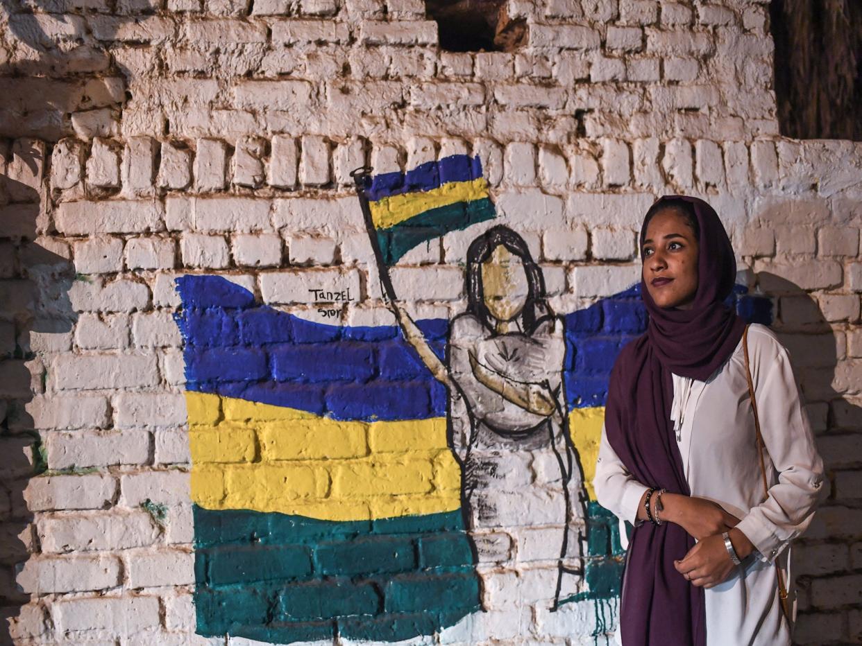 Sudanese protester, Alaa Salah, poses in front of a recently painted mural of a female protester during a demonstration near the army headquarters: AFP/Getty