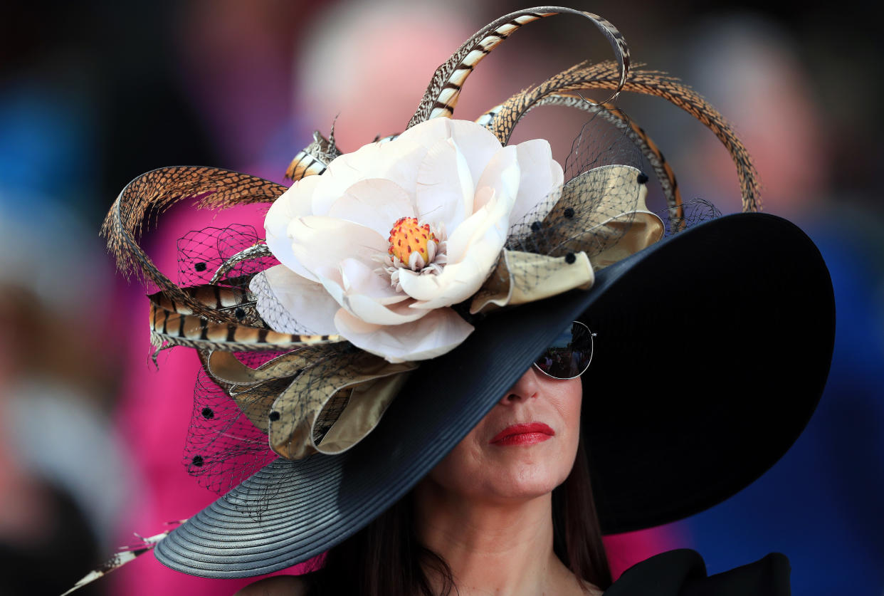 A woman's face is partially shielded by a large hat with many flowers and feathers.