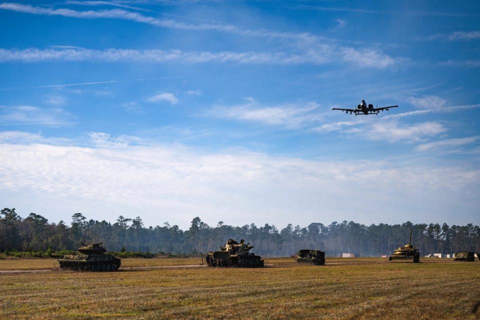 A gray fighter jet flies above a line of tanks