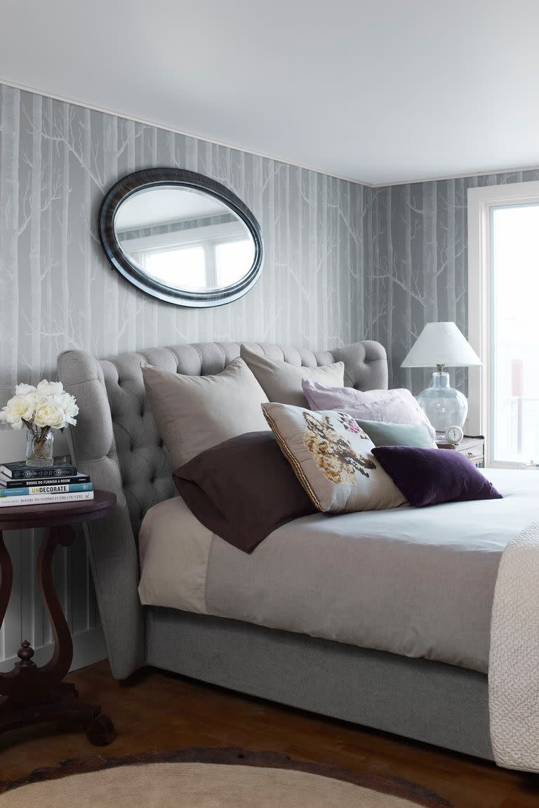 <p>Aside from the purple velvet throw pillows, this room is full of soothing variations of gray, everything from the wallpaper to the tufted headboard.</p>