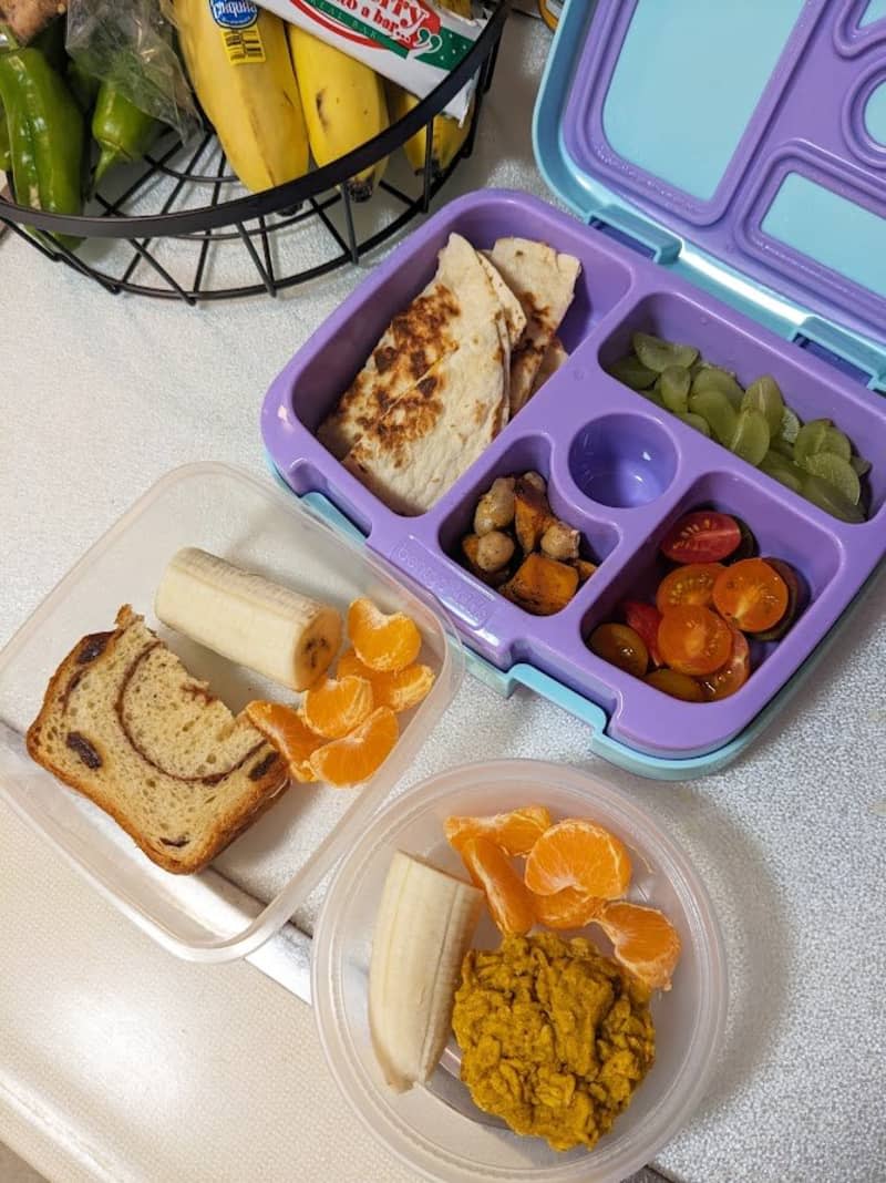 lunch boxes with compartments for cherry tomatoes, tangerines, half a banana, dried fruits, sandwich halves