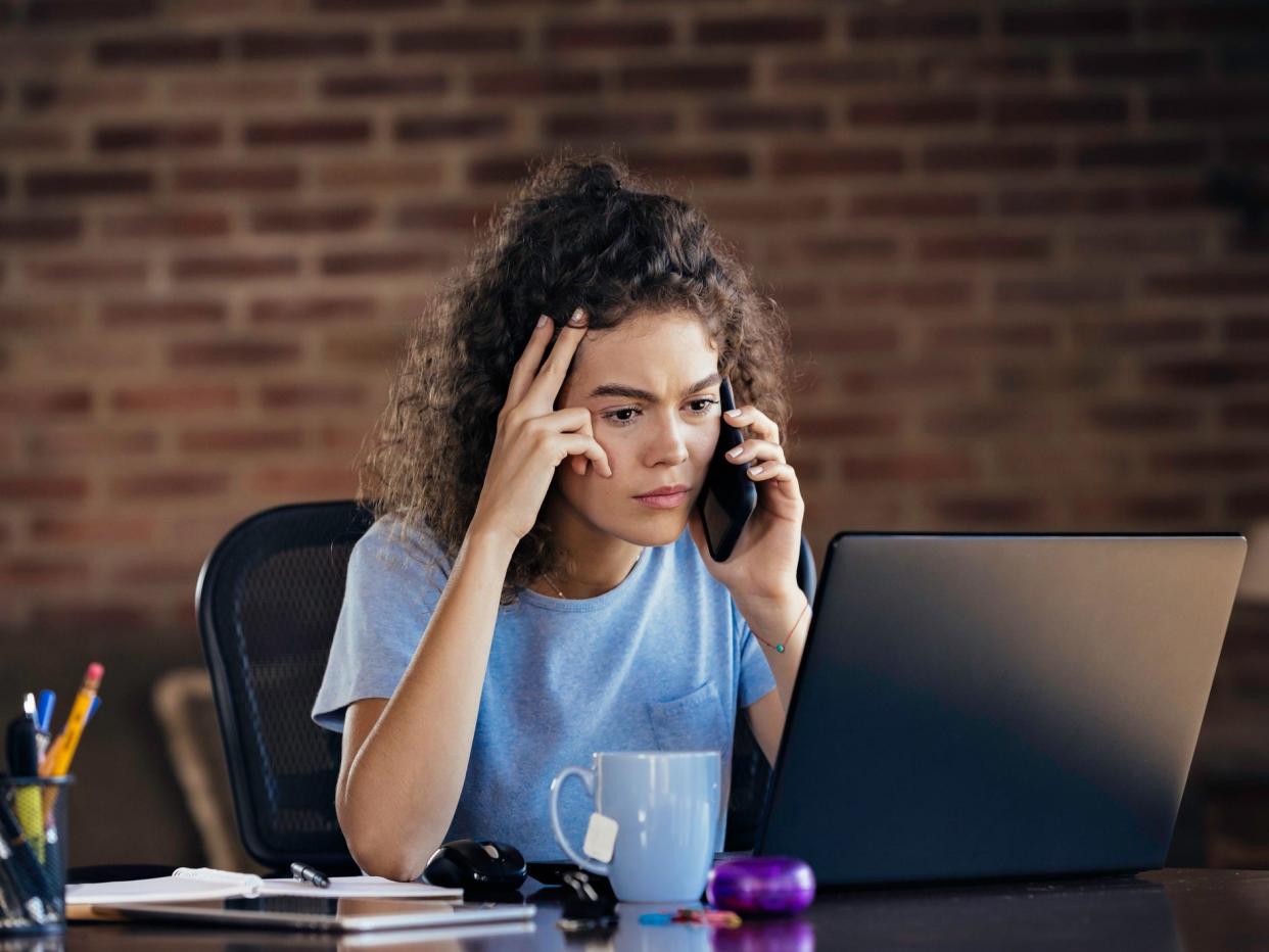 Curly haired woman working at laptop troubleshooting on the phone