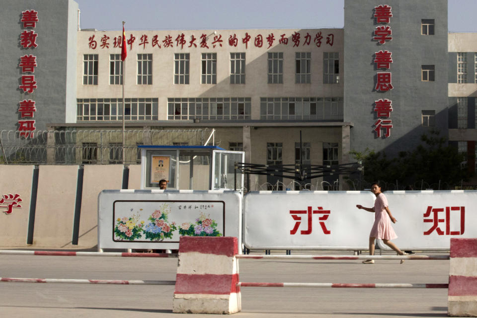 In this Aug. 31, 2018, photo, a woman walks past the Kashgar Dongcheng No. 4 Junior Middle School, which is part of a cluster of schools with slogans which read "Study hard to realize the Chinese dream of the great rejuvenation of the Chinese nation", "Kind Learning, Kind Thoughts, Kind Actions" and "Pursue Knowledge" on the outskirts of in Kashgar, western China's Xinjiang region. (AP Photo/Ng Han Guan)