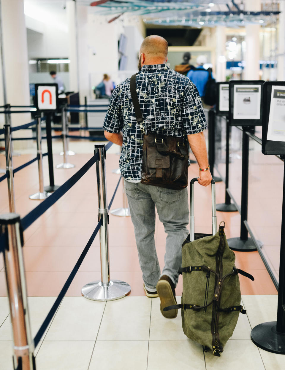 back of a person rolling their luggage in the airport