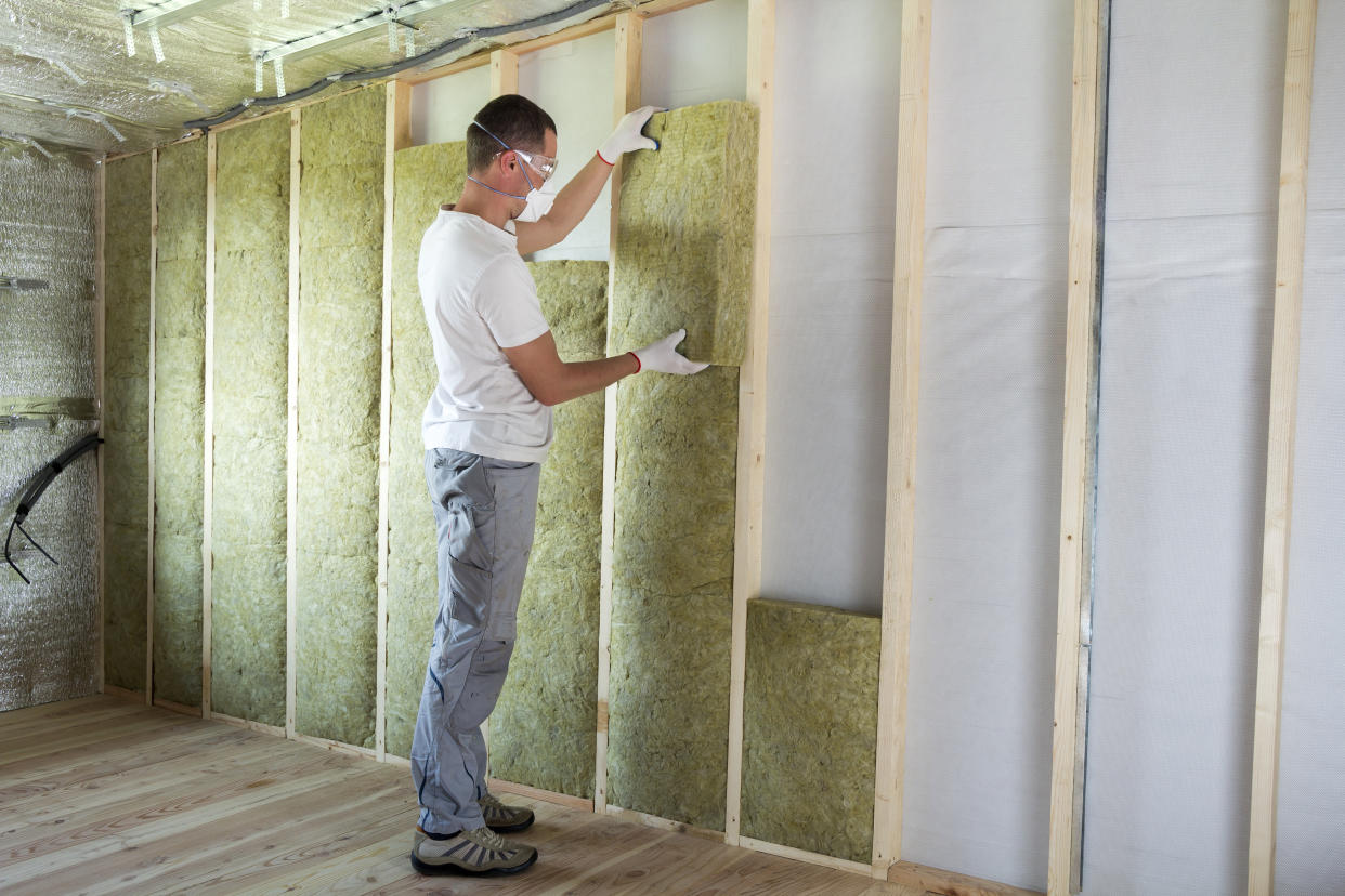 energy bills Worker in protective goggles and respirator insulating rock wool insulation in wooden frame for future house walls for cold barrier. Comfortable warm home, economy, construction and renovation concept