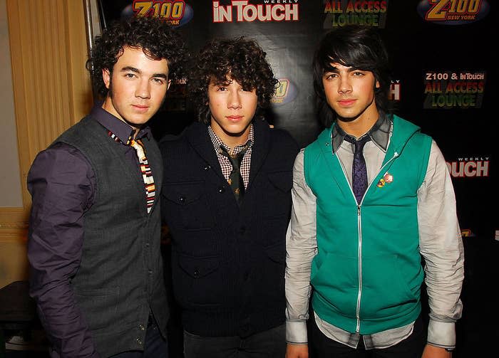 Joe wearing a long-sleeved shirt, tie, and a brightly colored jacket as he poses with his brothers for a photo