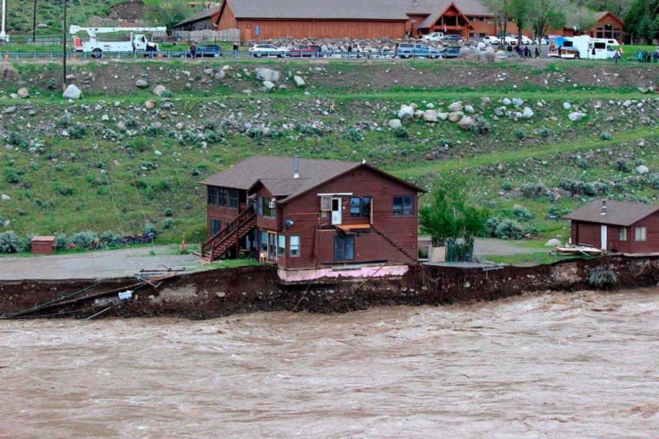 In this image provided by Sam Glotzbach, the flooding Yellowstone River undercuts the river bank, threatening a house and a garage in Gardiner, Mont., on June 13, 2022 (AP)