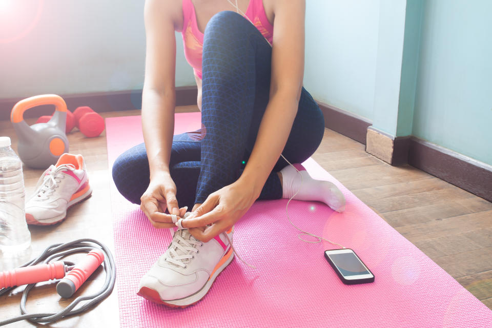 Woman tying her shoelaces on a workout mat from home