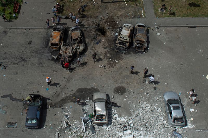 Personas junto a coches destruidos por un ataque de misiles rusos en Járkov