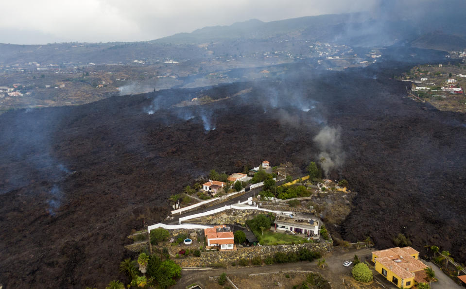 Lava from a volcano eruption flows destroying houses on the island of La Palma in the Canaries, Spain, Tuesday, Sept. 21, 2021. A dormant volcano on a small Spanish island in the Atlantic Ocean erupted on Sunday, forcing the evacuation of thousands of people. Huge plumes of black-and-white smoke shot out from a volcanic ridge where scientists had been monitoring the accumulation of molten lava below the surface. (AP Photo/Emilio Morenatti)