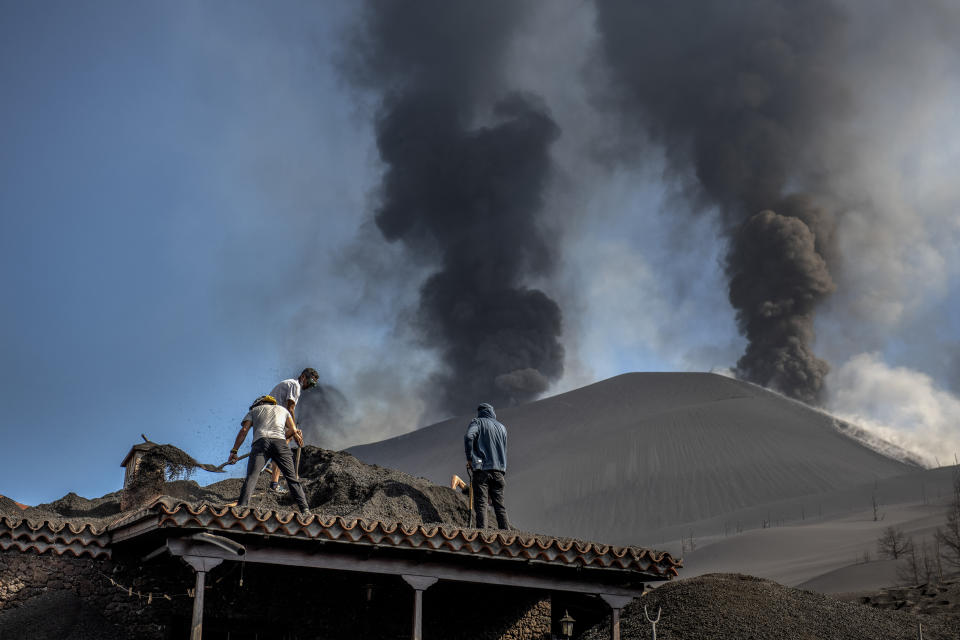 People clean up the ash off a house from the volcano in Las Manchas on the Canary island of La Palma, Spain on Thursday Oct. 14, 2021. Hundreds of people in Spain's Canary Islands are fearing for their homes and property after a new lava stream from an erupting volcano threatened to engulf another neighborhood on the island of La Palma. (AP Photo/Saul Santos)