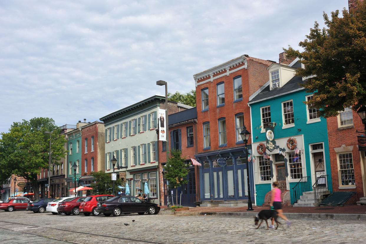 A young lady with a dog walking on brick paved street at Fell's Point in the city of Baltimore