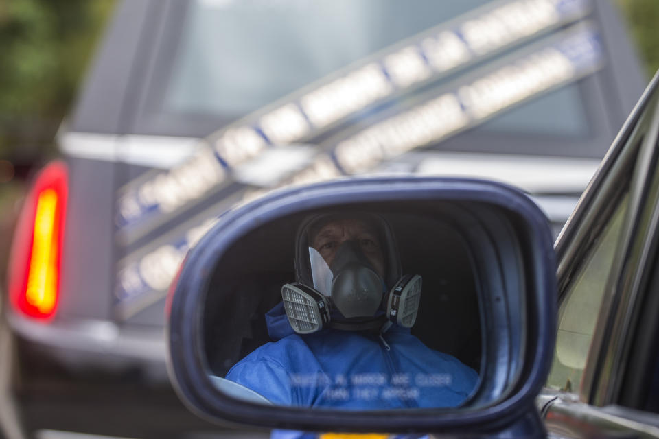 A driver wearing hazardous materials gear sits in a funerary car behind the hearse carrying the body of Dr. William Gutierrez, after arriving for his cremation at a cemetery in Bogota, Colombia, Sunday, April 12, 2020. Dr. Gutierrez, an anesthesiologist who was the head of the intensive care unit of the Olaya Polyclinical Center, died Saturday as a result of pneumonia produced by the new coronavirus, the Medical Federation of Colombia said. (AP Photo/Ivan Valencia)