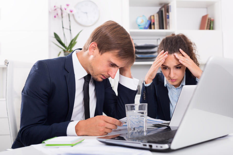 Professionally dressed man and woman at laptop, holding their heads