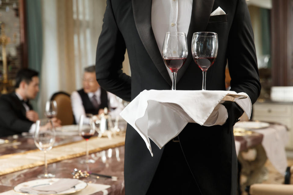 man in a tux holding a tray with two glasses of wine