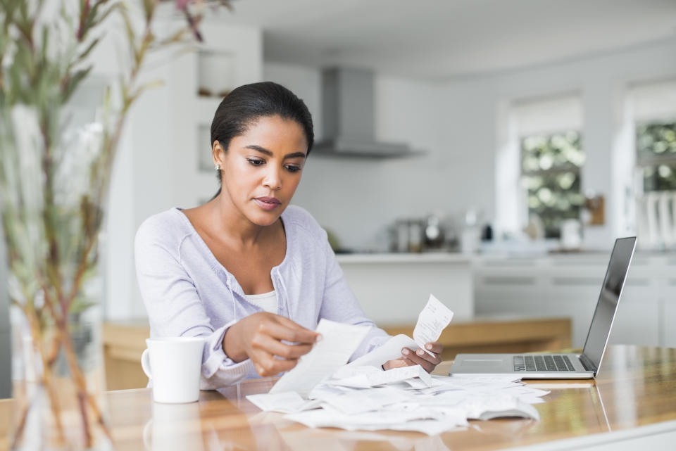 Mid adult woman reading bills while making online payment at home financial paperwork