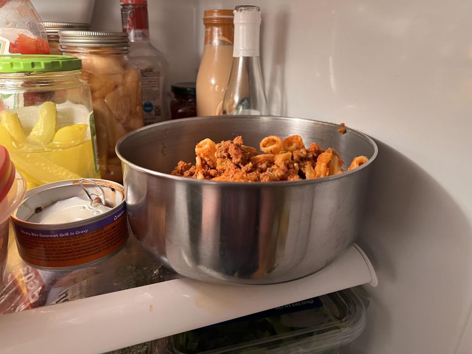 Bowl of pasta in a fridge among various condiments and a can