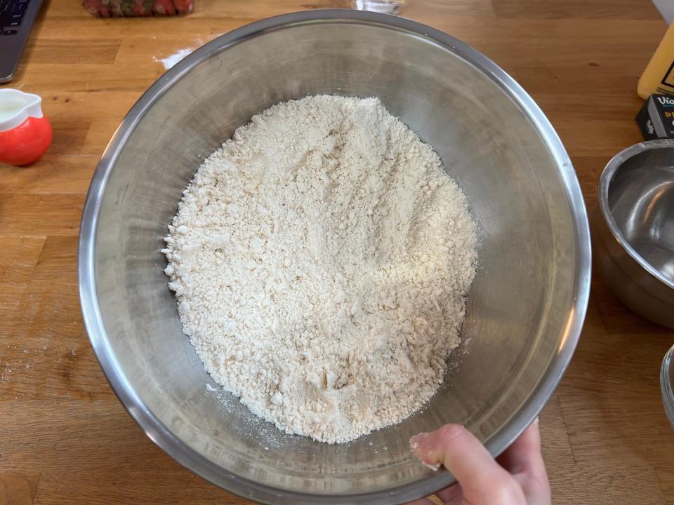 A hand holds a silver mixing bowl with a breadcrumb-like mixture inside.