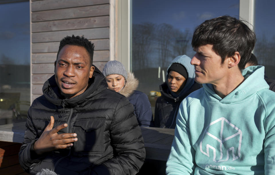 Emmanuel Oyedele, front left, and host Christian Vollmann, front right, speak to The Associated press in Gross Koeris near Berlin, Germany, Monday, March 7, 2022. Vollmann offered his holiday home until the end of April to the Nigerian students who fled Kyiv after the Russian attack on Ukraine. (AP Photo/Michael Sohn)
