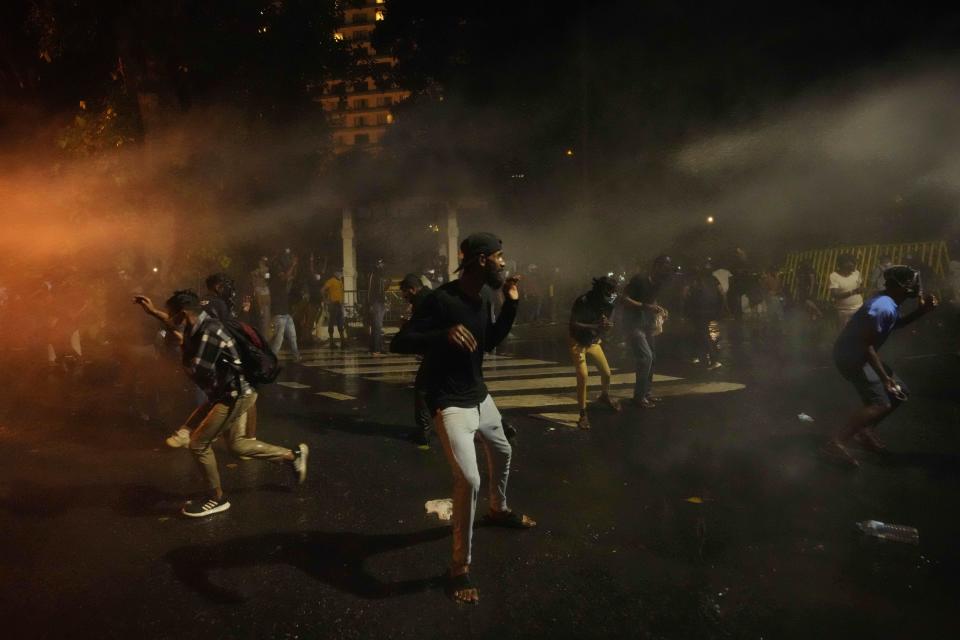 Protesters run for cover as police fire tear gas shells near the president's official residence in Colombo, Sri Lanka, Saturday, May 28, 2022. Police fired tear gas and water canon on protesters who marched toward the president Gotabaya Rajapaksa's barricaded residence demanding his resignation. (AP Photo/Eranga Jayawardena)