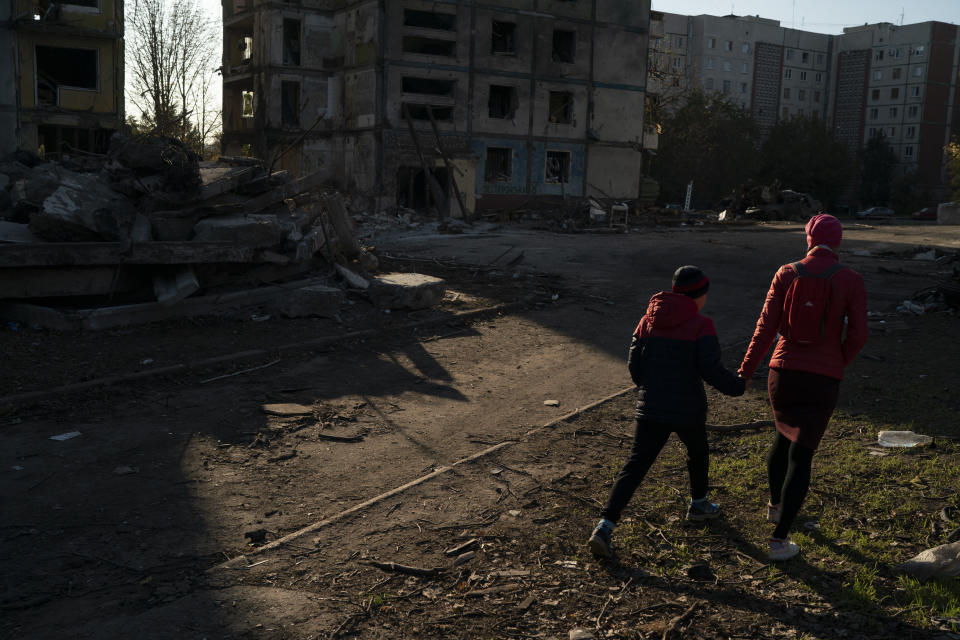 A woman holds the hand of her son as they walk past residential building that was heavily damaged after a Russian attack last week in Zaporizhzhia, Ukraine, Sunday, Oct. 16, 2022. (AP Photo/Leo Correa)