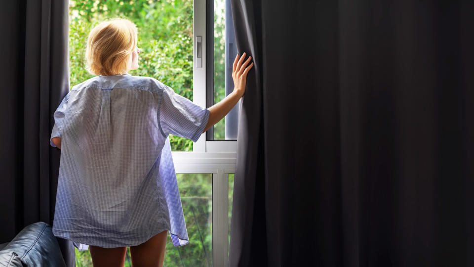 A person opening a set of blackout curtains