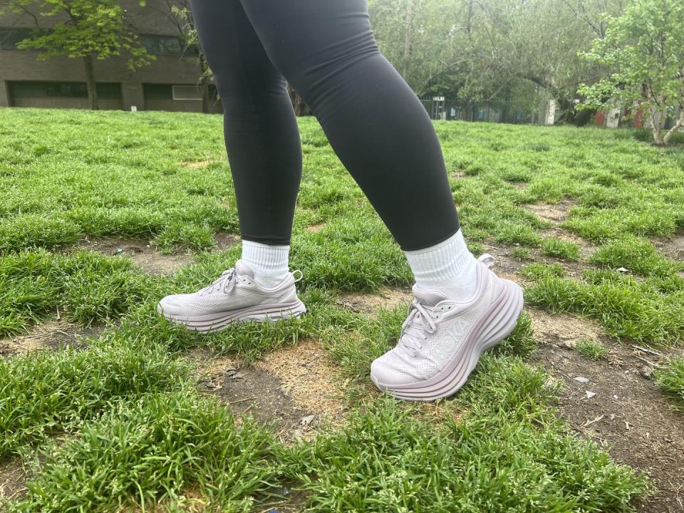 a model wearing purple hoka bondi 8 sneakers on a grassy field, good housekeeping's pick for best cushioned walking shoes for women