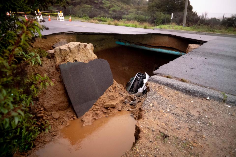 One of two cars trapped in a large sinkhole is visible along Iverson Road in Chatsworth, Calif., on Jan. 10, 2023.