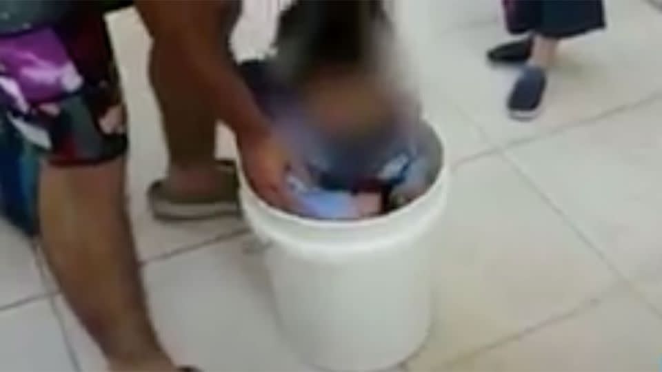 The petrified screams of the infant can be heard as her father forces her inside a white bucket. Photo: Israeli News Flash