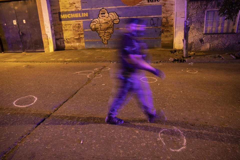 A police officer walks amid circles marking spent bullet shells after a fight between criminal gangs for the control of territory in Rosario, Argentina, Friday, Dec. 3, 2021. The city of some 1.3 million people has high levels of poverty and crime, where violence between gangs who seek to control turf and drug markets has helped fill its prisons. (AP Photo/Rodrigo Abd)