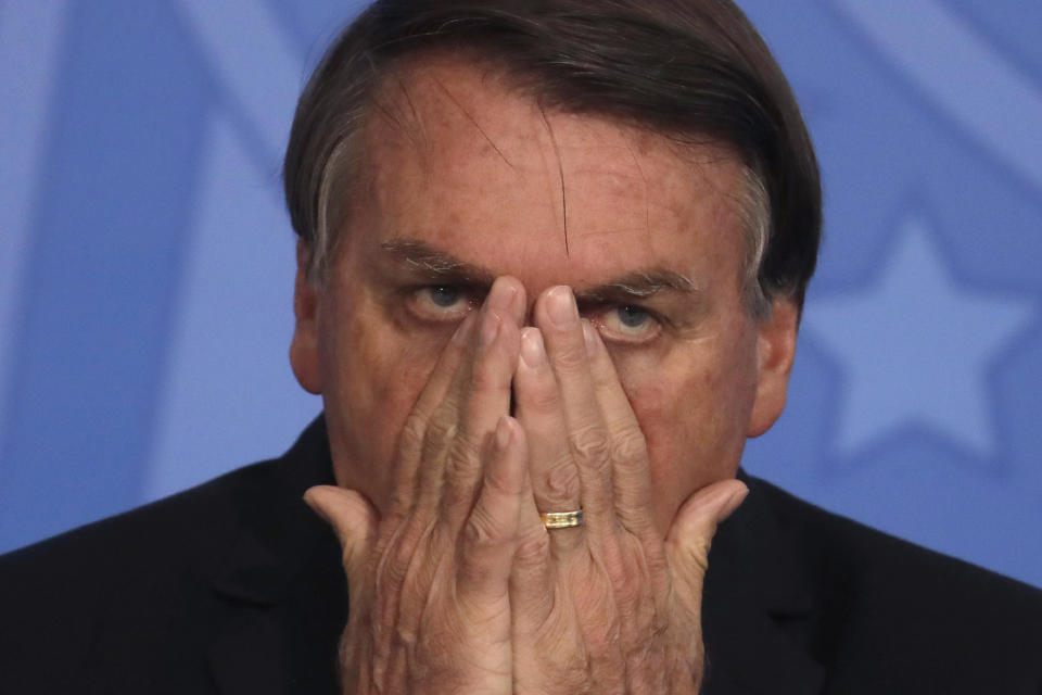 Brazil's President Jair Bolsonaro passes his hand over your face during a ceremony at the Planalto presidential palace, in Brasilia, Brazil, Thursday, Nov. 26, 2020 (AP Photo/Eraldo Peres)