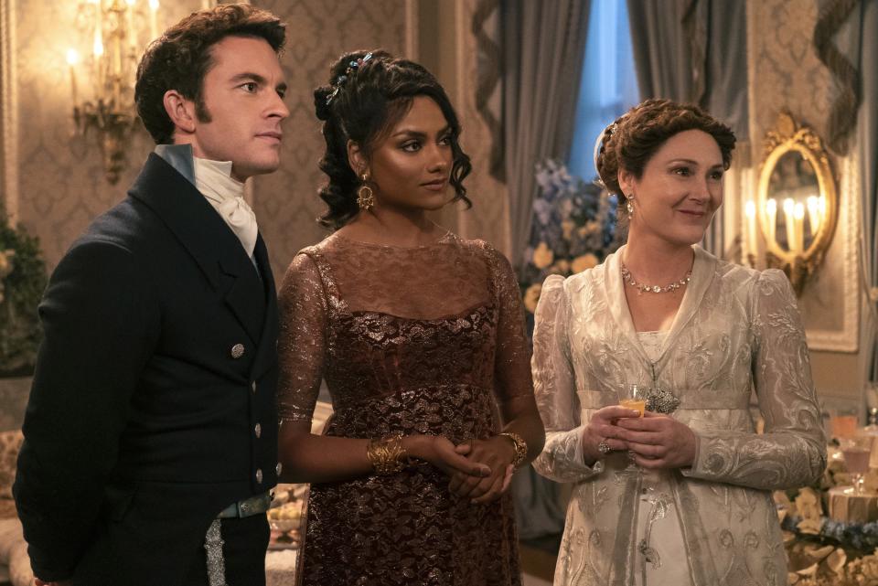 Jonathan Bailey, Simone Ashley and Polly Walker stand together at an official event, dressed in period costumes