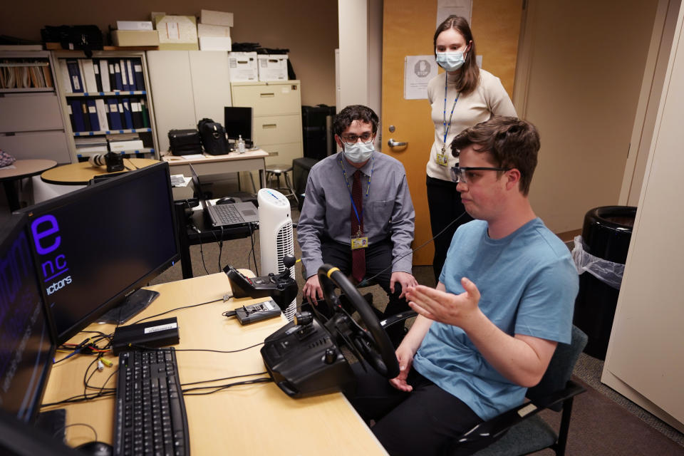 Tate Ellwood-Mielewski, right, talks with research technicians Joseph Levin, left, and Cameron Perrin before a simulator test drive at the University of Michigan, Friday, April 29, 2022, in Ann Arbor, Mich. Michigan researchers plan to study how well those with autism spectrum disorder detect road hazards and assist the young motorists in sharpening their driving skills. The upcoming effort marks the second phase of a project that is funded by Ford Motor Co. and teams the Ann Arbor university with a local driving school. (AP Photo/Carlos Osorio)