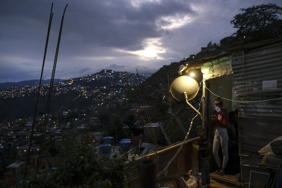 A woman looks at her smartphone outside of her home in the El Quilombo neighborhood of Caracas, Venezuela, Saturday, Feb. 13, 2021, amid the new coronavirus pandemic. (AP Photo/Matias Delacroix)