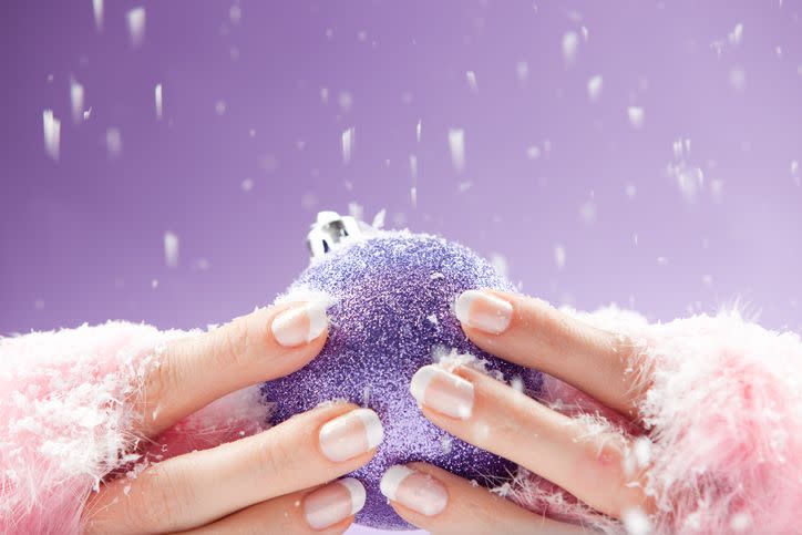 womans hand in fingerless puffy gloves holding a christmas bauble