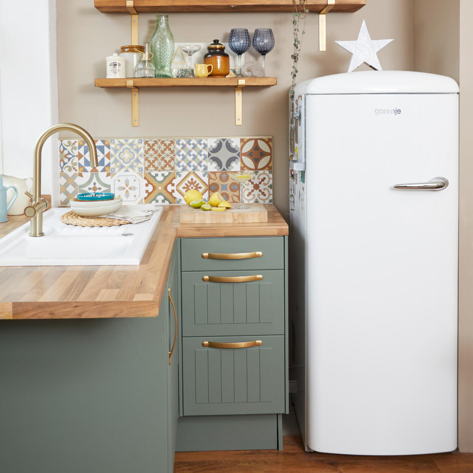 Green painted kitchen cabinets with gold brass handles, wooden worktop, and fridge