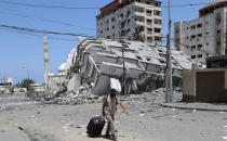 A man pulls his luggage while passing the rubble of a destroyed building which was hit by Israeli airstrikes, in Gaza City, Wednesday, May 12, 2021. (AP Photo/Adel Hana)