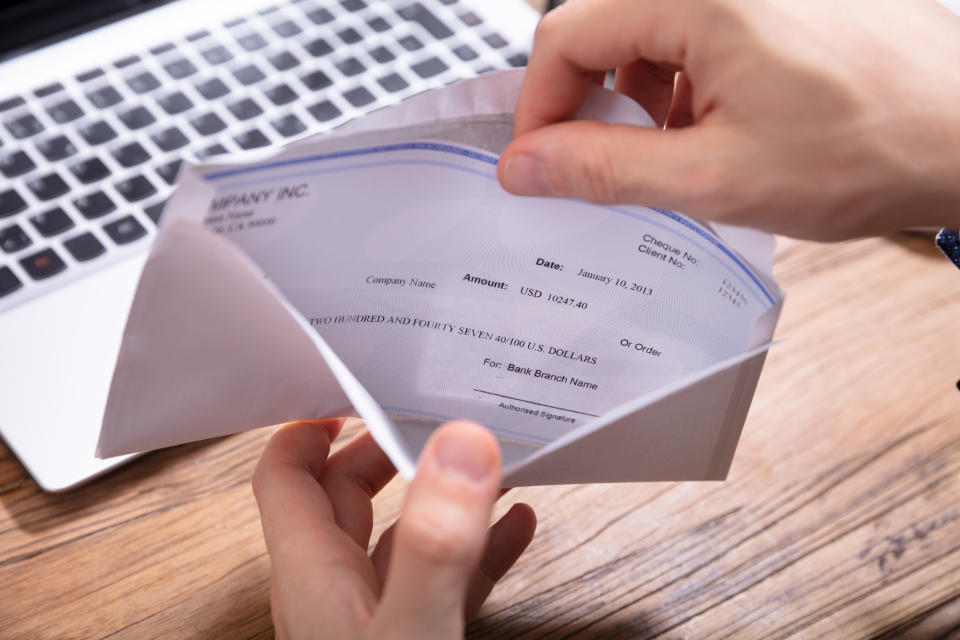 Elevated View Of Person's Hand Removing Paycheck From The Envelope Over Wooden Desk