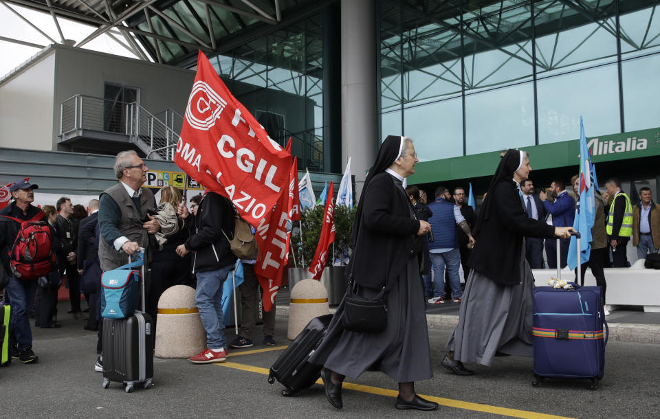 Nuns and other passengers pass in front of striking Alitalia workers with unions flags and banners, at the Fiumicino airport in Rome Tuesday, May 21, 2019. Alitalia workers are on a 24 hours strike since Monday night. (AP Photo/Allessandra Tarantino)