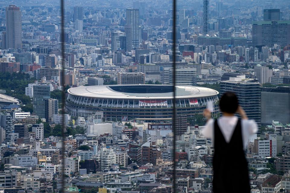 A person wearing a protective mask takes a picture from an observation deck as National Stadium, where the opening ceremony of the Tokyo Olympics will be held, is seen in the background.