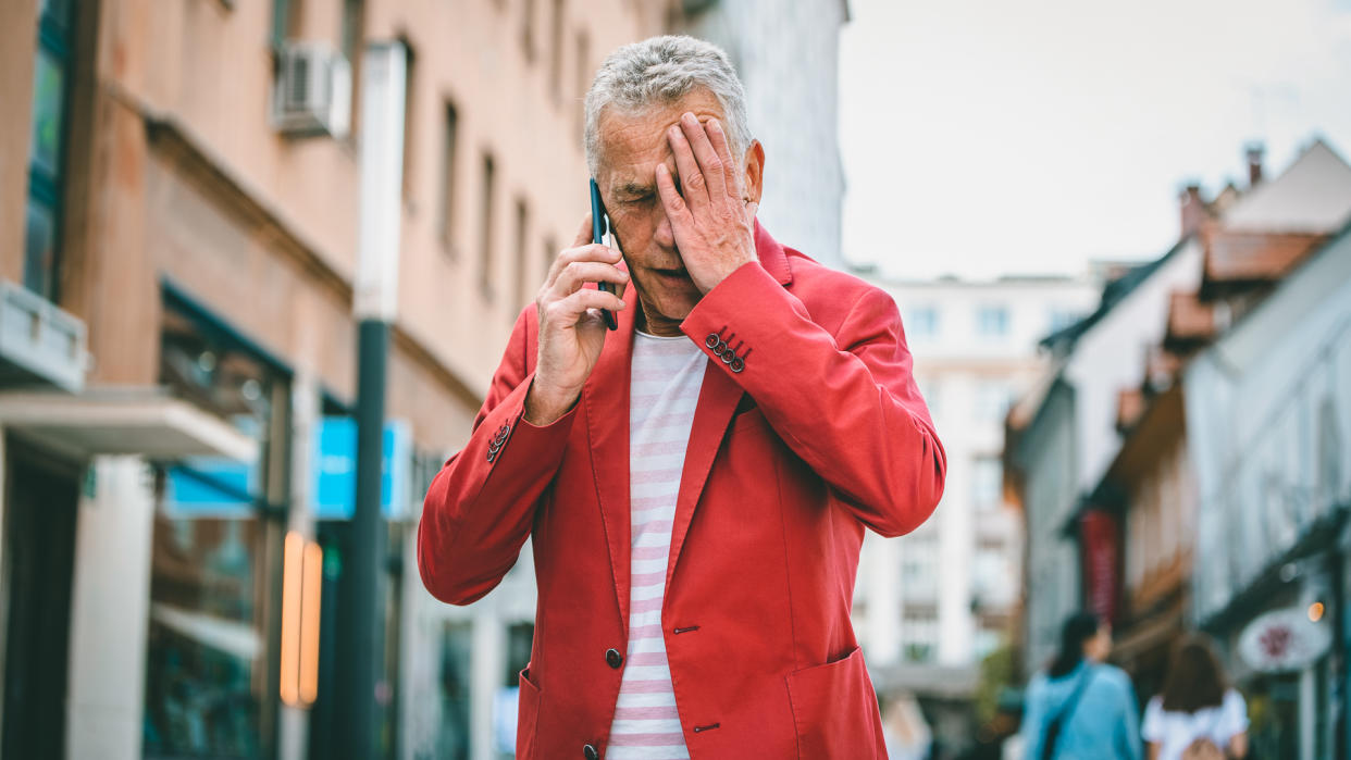 Low angle front view close-up of Caucasian man in early 60s learning bad news as he pauses to take an outdoor call during city break in Ljubljana.