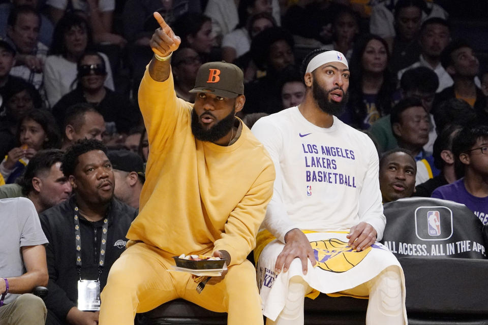Los Angeles Lakers forward LeBron James, left, gestures to fans as he sits on the bench with forward Anthony Davis during the second half of an NBA preseason basketball game against the Golden State Warriors Friday, Oct. 13, 2023, in Los Angeles. (AP Photo/Mark J. Terrill)