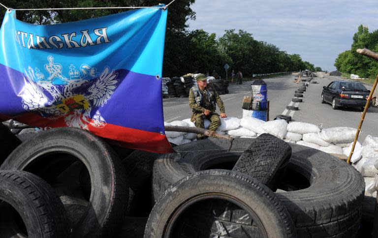 A pro-Russian militant sits as a flag of the self-proclaimed "Lugansk People's Republic" hangs at a checkpoint on the road between Lugansk and Donetsk on July 9, 2014