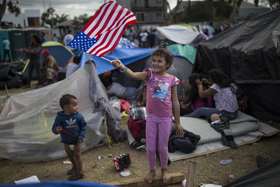 Seven-year-old Honduran migrant Genesis Belen Mejia Flores waves an American flag at U.S. border control helicopters flying overhead near the Benito Juarez Sports Center serving as a temporary shelter for Central American migrants, in Tijuana, Mexico, Saturday, Nov. 24, 2018. The mayor of Tijuana has declared a humanitarian crisis in his border city and says that he has asked the United Nations for aid to deal with the approximately 5,000 Central American migrants who have arrived in the city. (AP Photo/Rodrigo Abd)