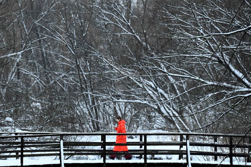 A woman walks across a bridge over the Yauza river in front of snow-covered trees after a snowfall in outskirts of Moscow on January 10, 2022.